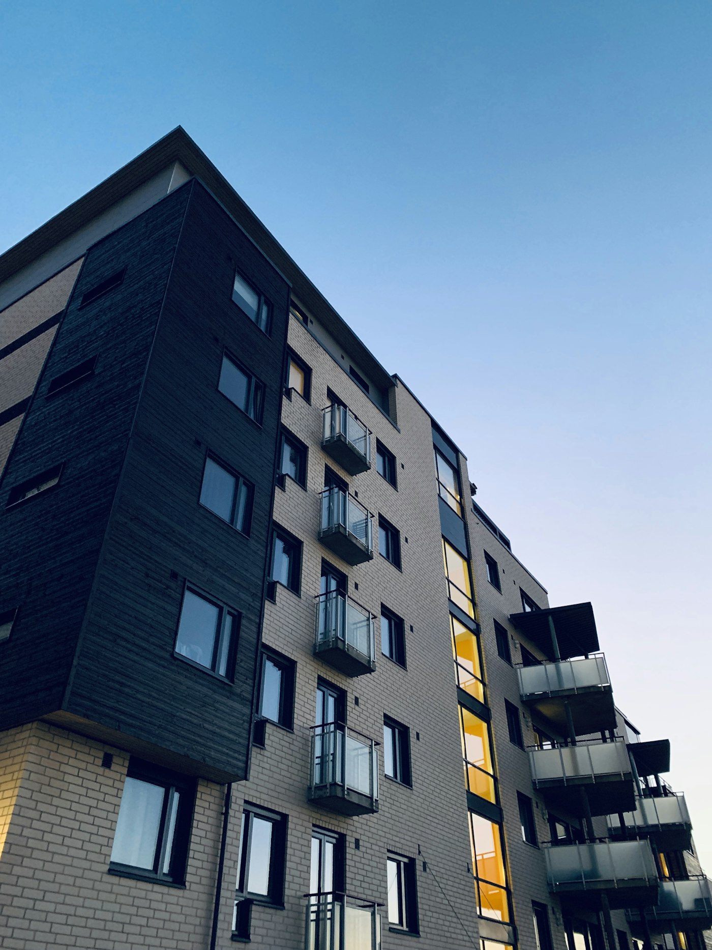 Edificio de departamentos moderno visto desde abajo, con balcones y fachada de ladrillo claro.