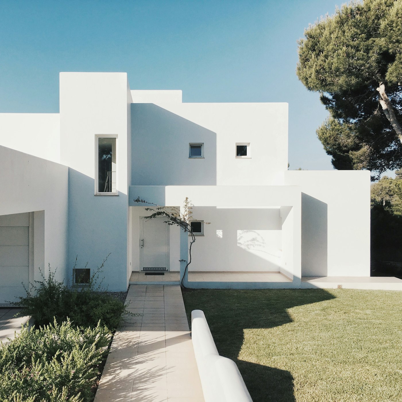 Casa moderna blanca de dos plantas con jardín, luz de día.